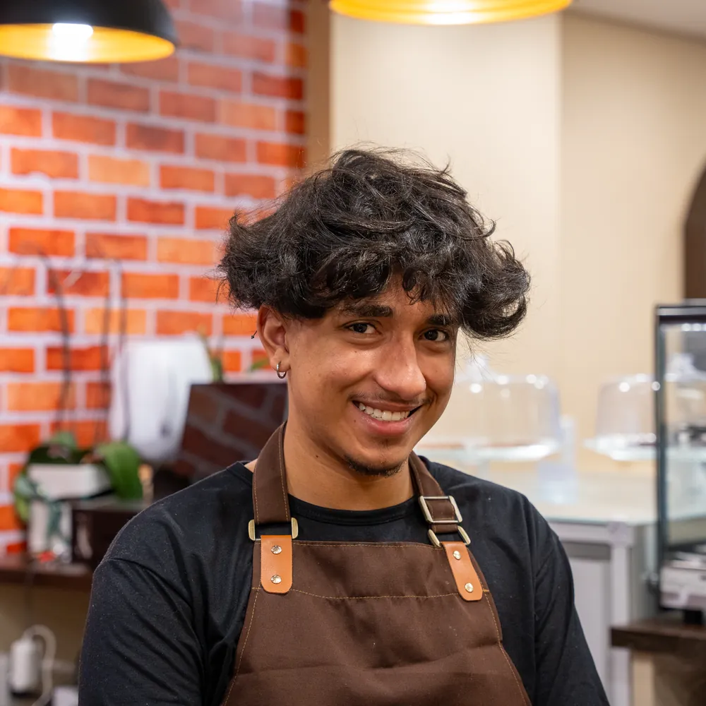 Barista da Cheirin Bão Anchieta sorrindo diante da parede de tijolinho